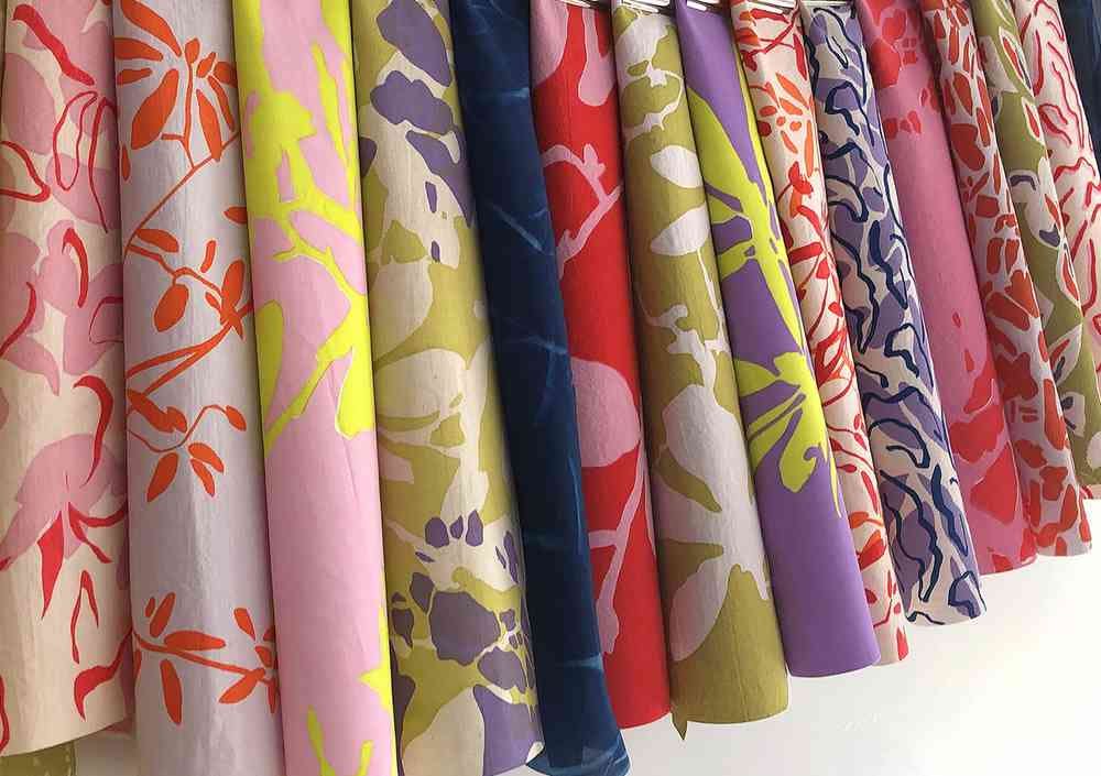 Photograph of rolls of colourful flower-patterned fabrics lined together. The colours include creams, yellows, pinks, greens and lilacs.