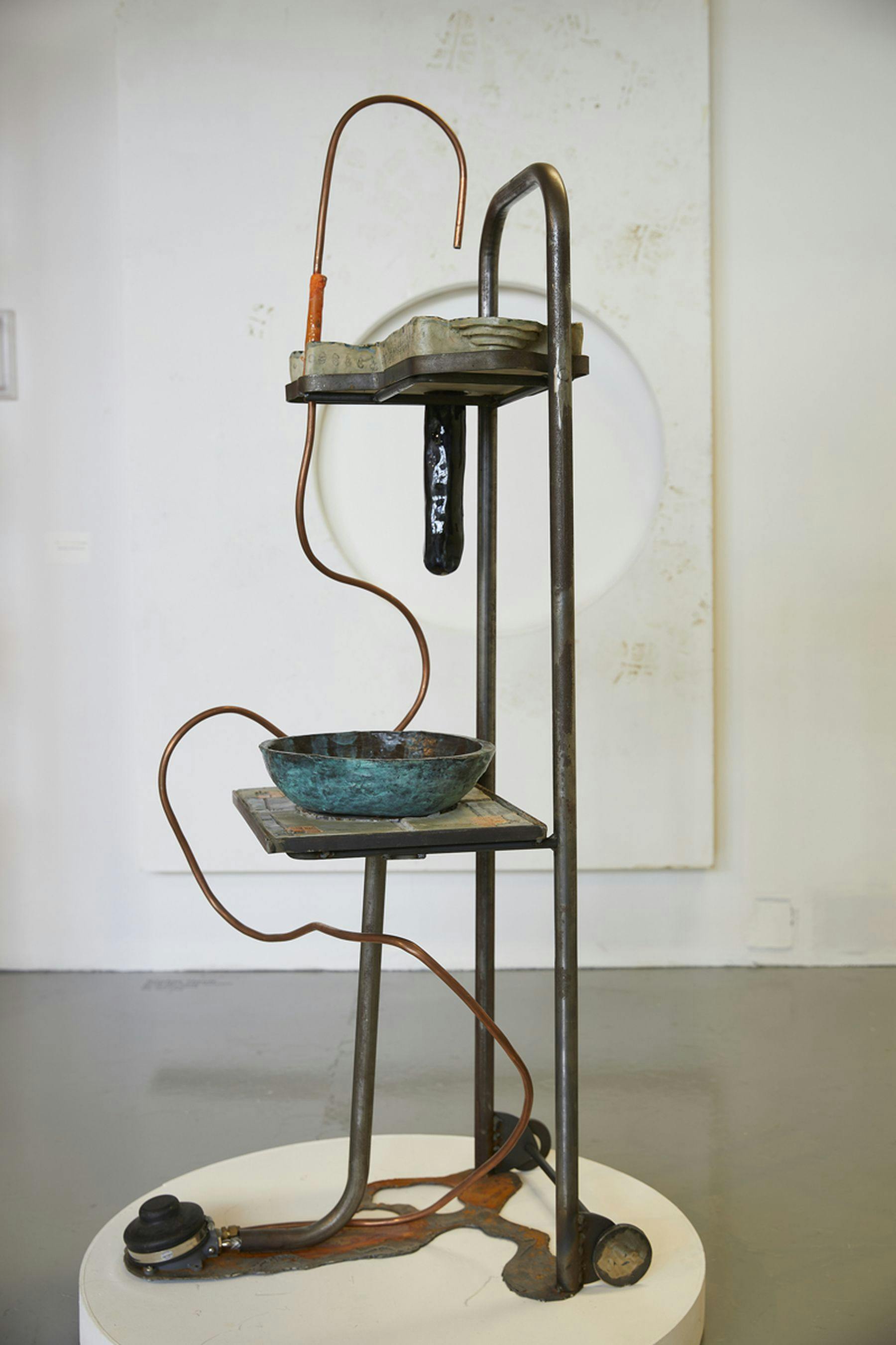 A photograph of a metal structure featuring a copper wire hook. Attached is a shelf with a blue bowl.