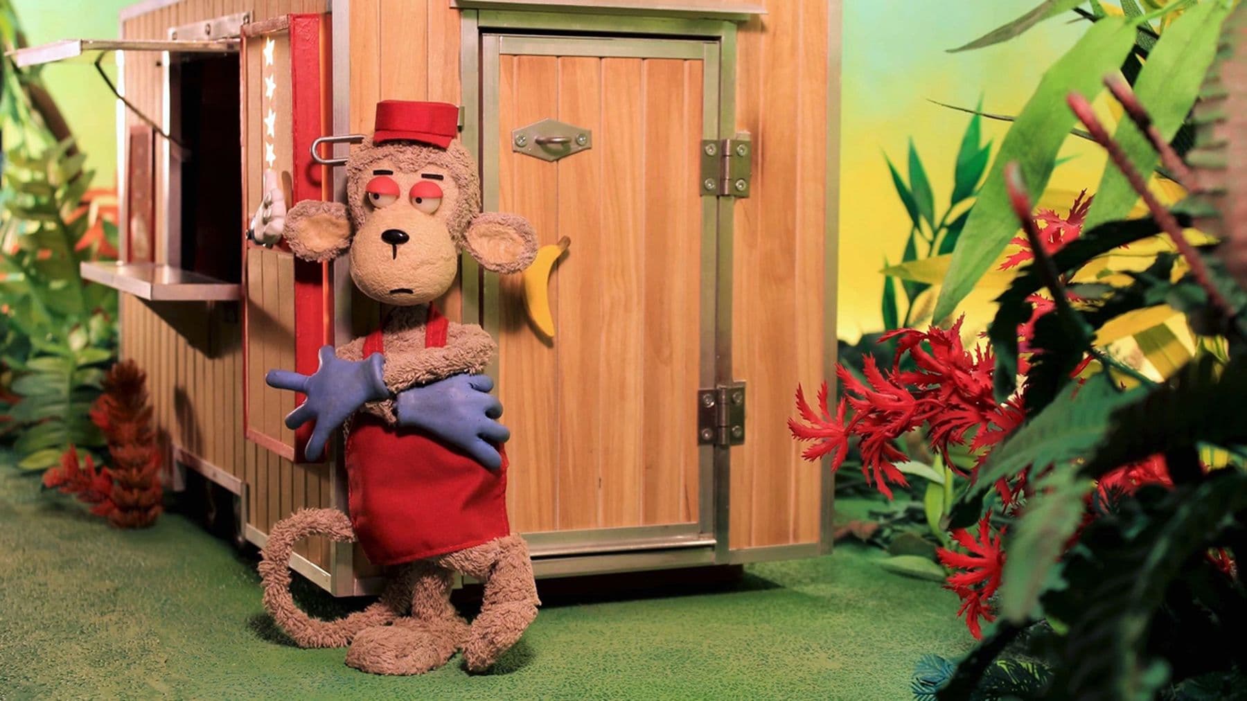 A stop motion still of a character in a red apron and purple gloves with its arms crossed. It stands against a wooden cabin surrounded by flowers and greenery.