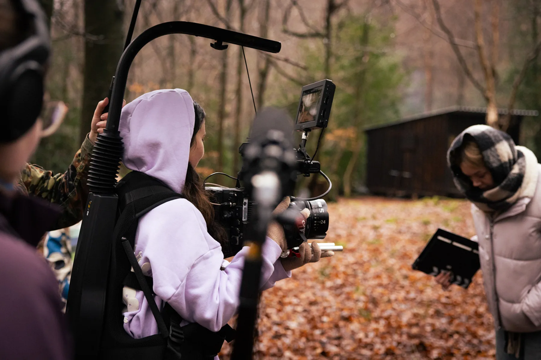 A photograph of people filming outdoors in autumn surrounded by fallen leaves with a camera operator and a person holding a clapperboard.