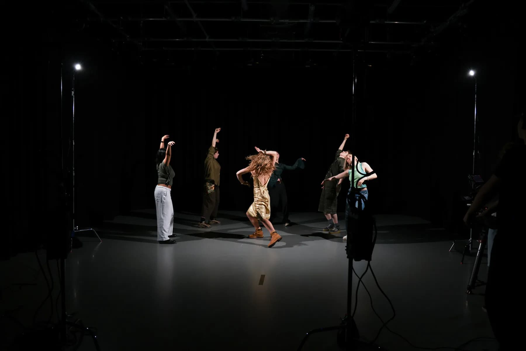 A photograph of a group of people dancing energetically on a dimly lit stage, each striking unique poses with raised arms and dynamic movements.