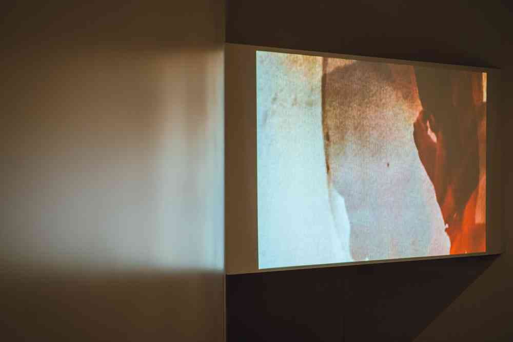 A photograph taken of a screen with an abstract image of colours mixed together. Part of the image features a wall on the left-hand side.
