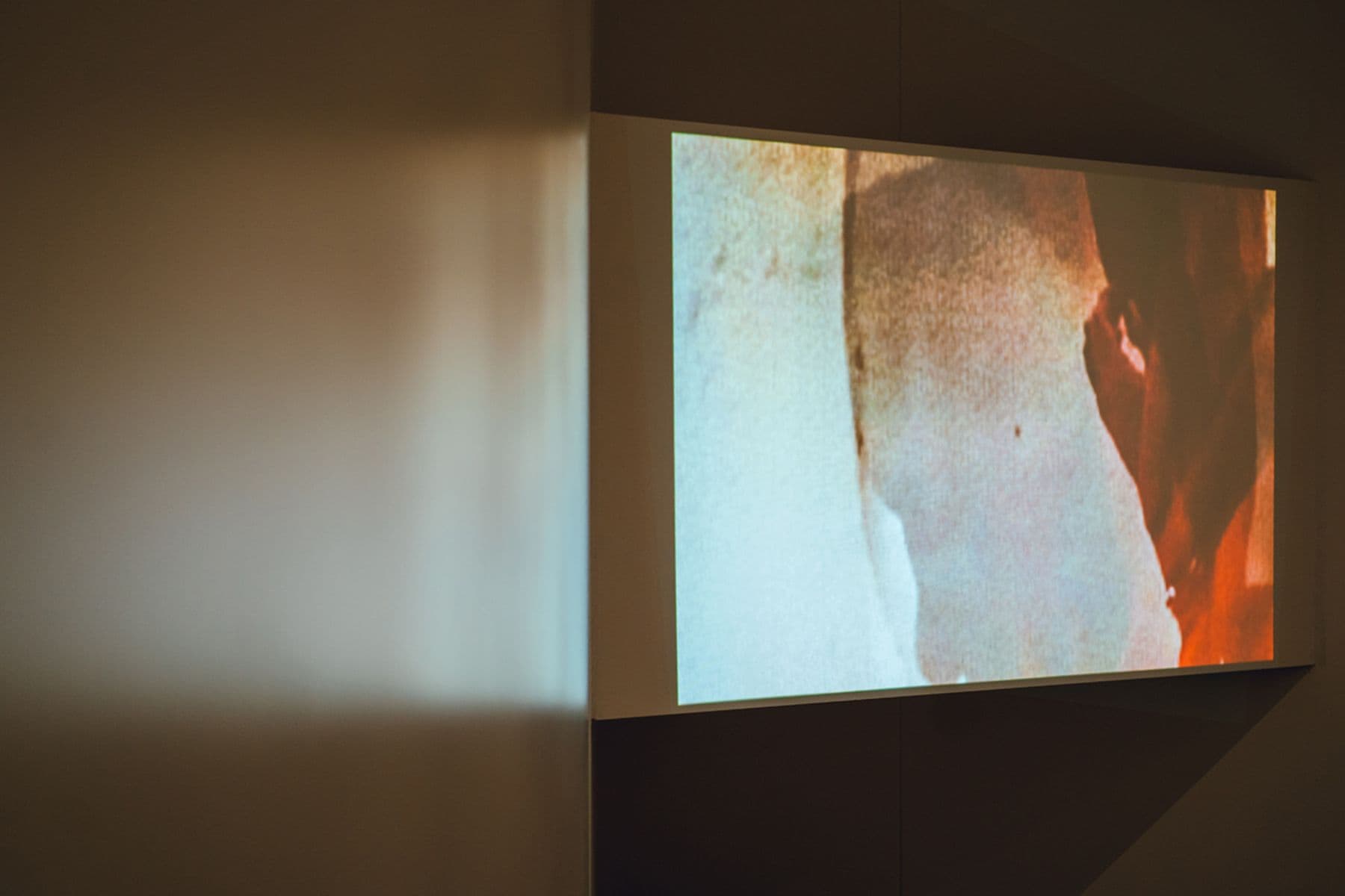 A photograph taken of a screen with an abstract image of colours mixed together. Part of the image features a wall on the left-hand side.