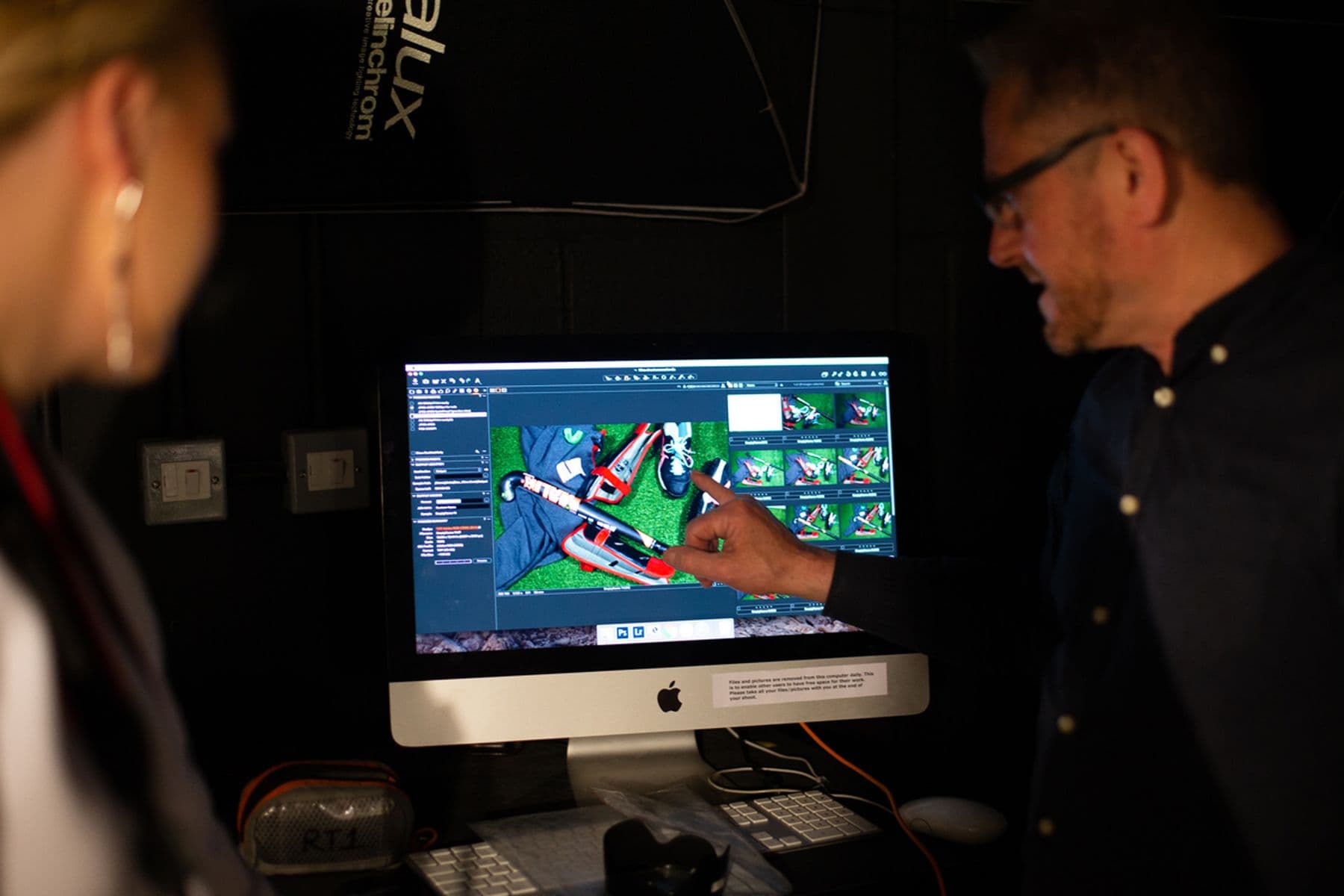 Two people discuss a computer screen displaying a 3D model of a red object.