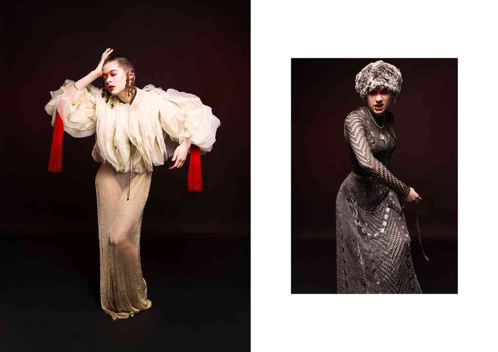 A photograph of two models dramatically posing. One is wearing  a voluminous cream outfit with red accents and another is wearing an ornate dark dress with a fur hat, against a black background.