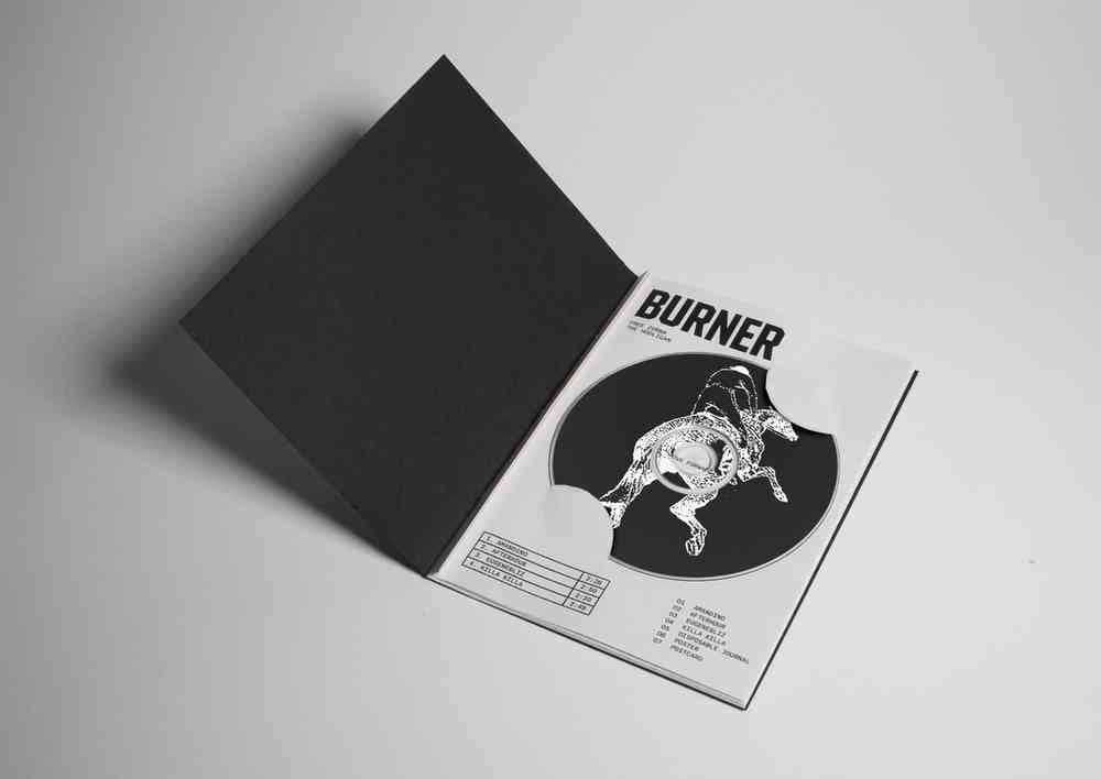 A photo of a printed magazine titled Burner. The magazine is black and white and there is a CD in the centre with an illustration of someone riding a rearing horse.