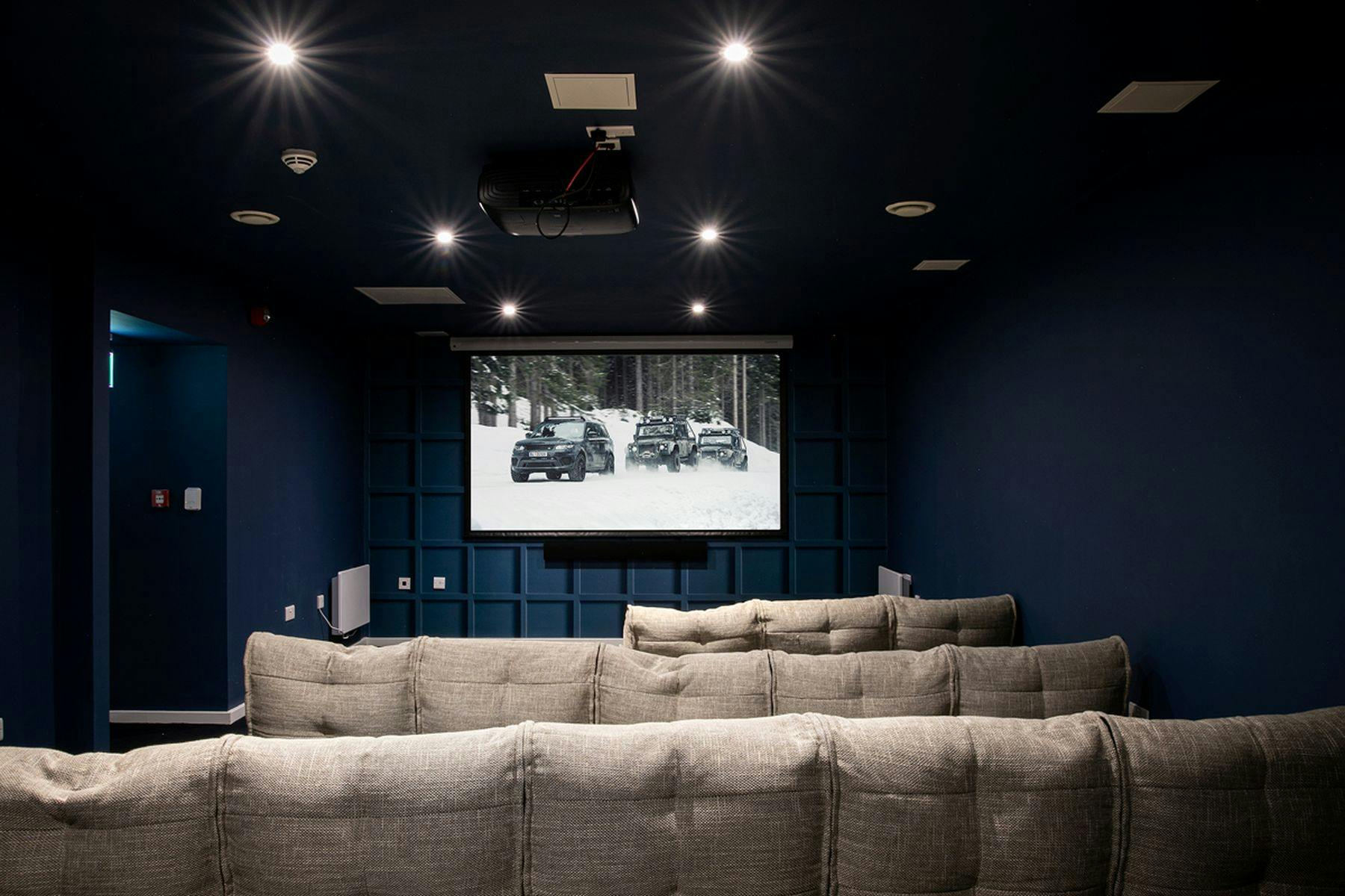 A photograph of the The Leather Works cinema room, it features a large screen with blue panelled walls and beige sofas.