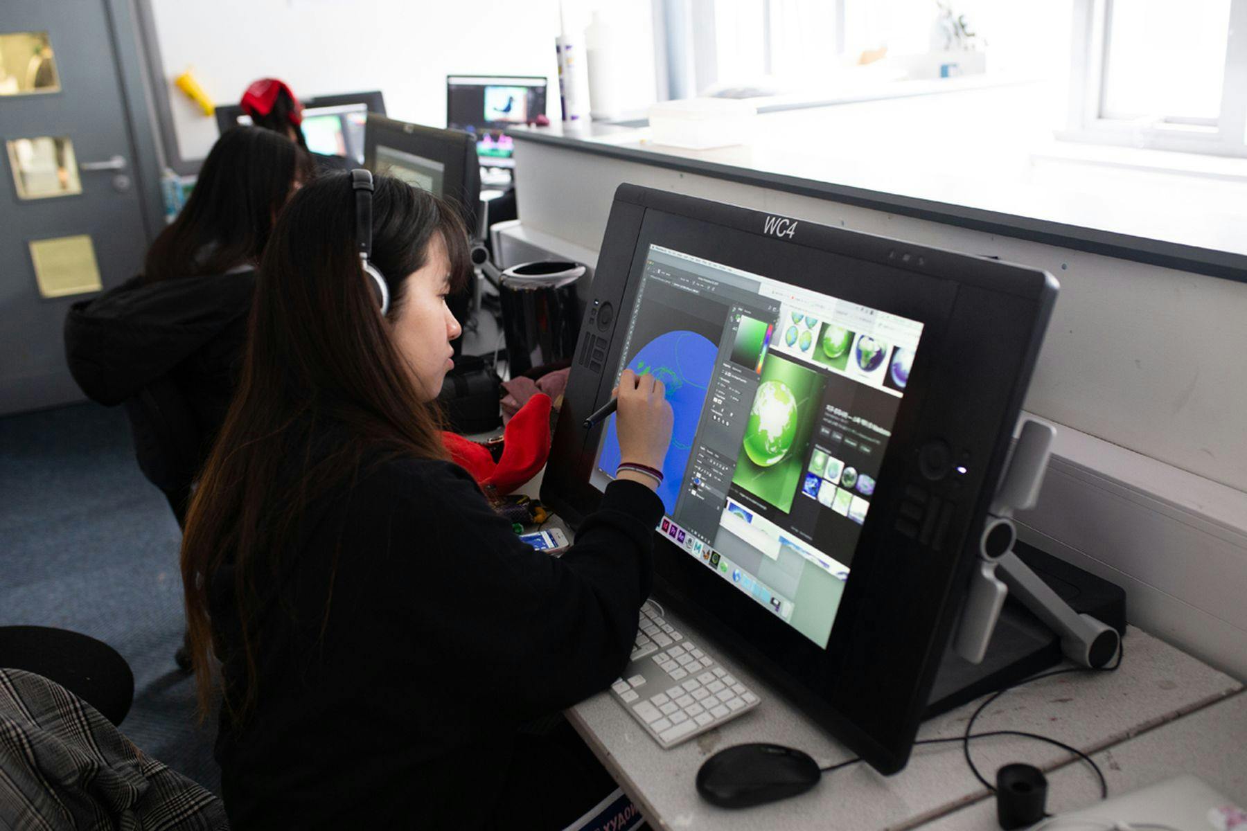 Photograph of a student drawing on Wacom tablet whilst wearing headphones.
