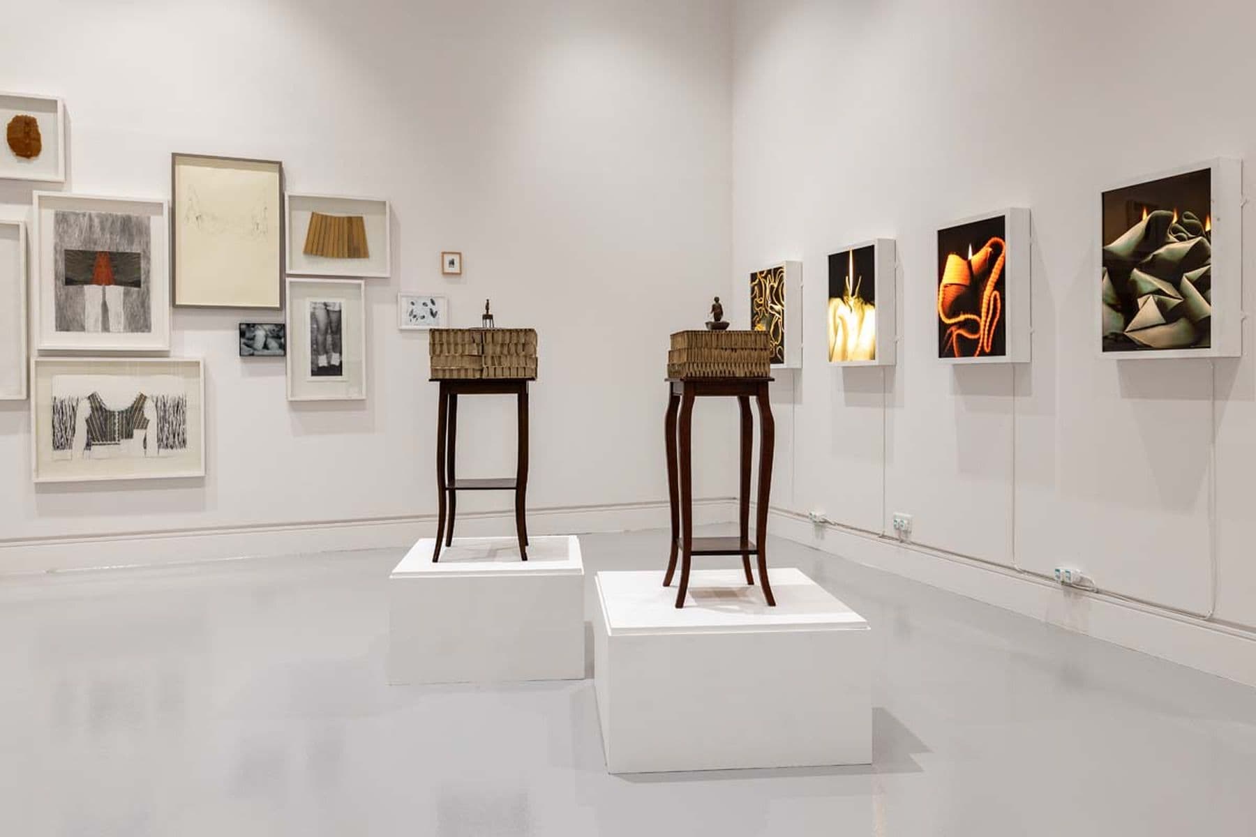 A photograph of a room with two wooden tables holding boxes and a foment, with framed prints in the background.