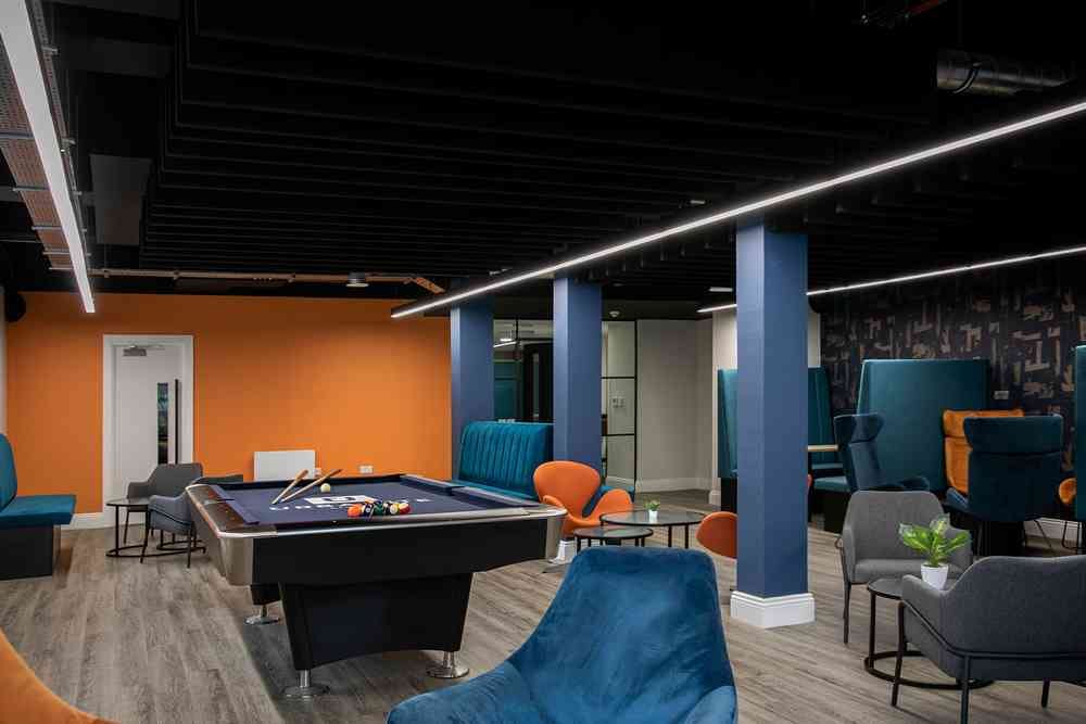 A photograph of The Leather Works accommodation communal area with a pool table and orange and blue seating.
