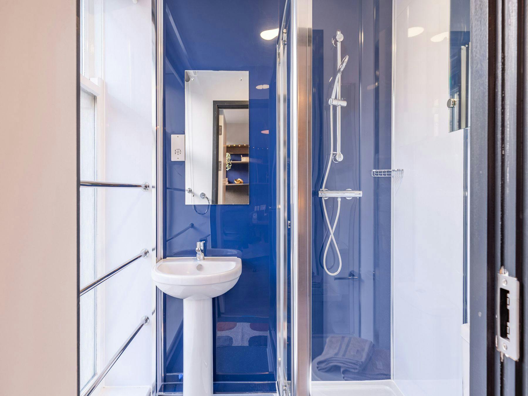 A photograph of The Leather Works deluxe ensuite with a blue reflective wall, mirror, sink and shower.